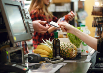 A customer handing a credit card at a grocery store checkout line. Groceries are more expensive due to price controls.