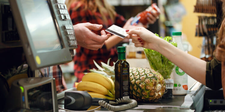 A customer handing a credit card at a grocery store checkout line. Groceries are more expensive due to price controls.