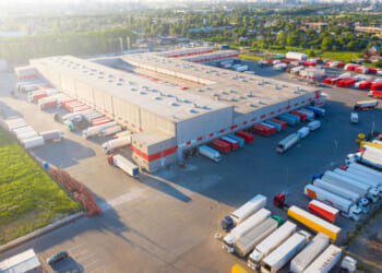 An aerial view of a warehouse with semi-trucks loading and leaving. Tariff policies have a negative effect on American businesses in trade.