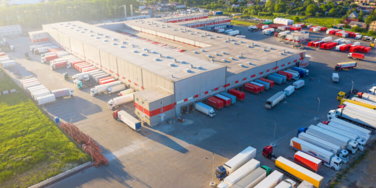 An aerial view of a warehouse with semi-trucks loading and leaving. Tariff policies have a negative effect on American businesses in trade.