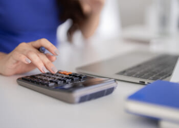 Someone doing their taxes, at a laptop with a calculator. Stress is due to Kansas' high taxes at multiple levels, and the state should focus on tax competitiveness.