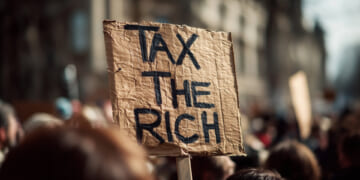 Tax the rich sign held up over a protesting crowd.