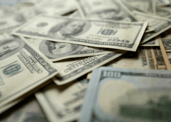 Close-up of a scattered pile of U.S. dollar bills, primarily $100 denominations, symbolizing government spending and fiscal policy in Kansas. The image highlights the concept of dedicated funds and their impact on accountability and transparency in public finance, as discussed in the Kansas Policy Institute article on undermining accountability in government budgets.
